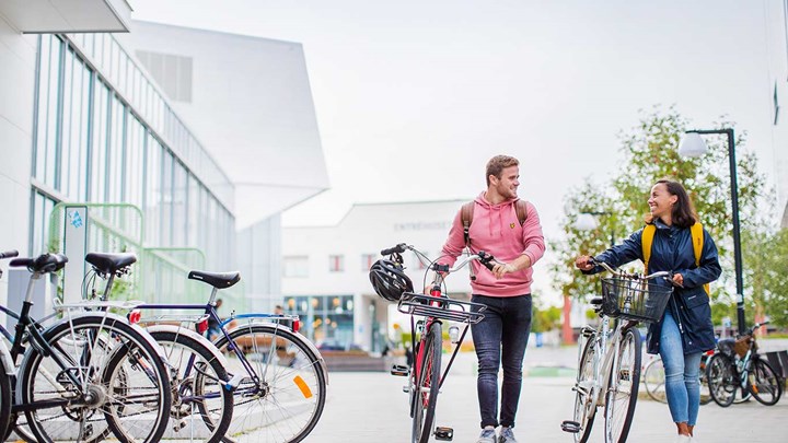 Två studenter går tillsammans på campus med sina cyklar.
