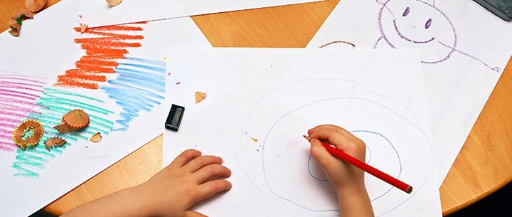 Två händer ritar barnteckningar vid ett bord