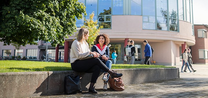 Två studenter sitter utomhus i solen på campus Örebro.
