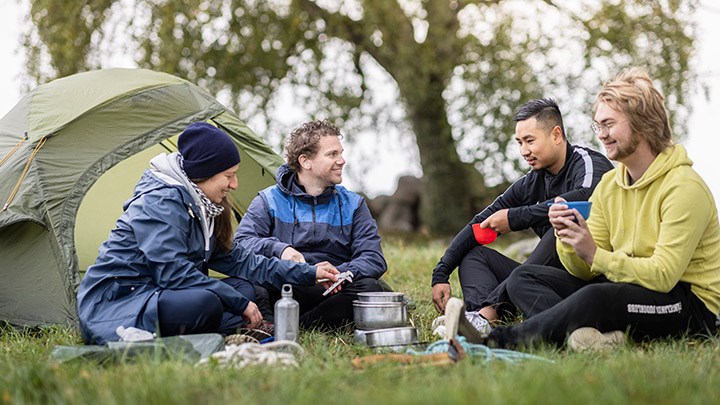 Fyra studneter sitter vid ett grönt tält i naturen.