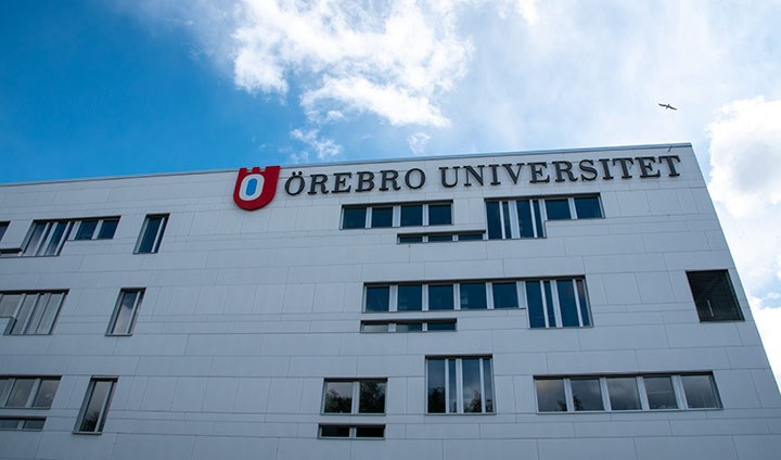 Det vita Novahuset mot en blå himmel. På fasaden sitter en skult med texten "Örebro universitet". 