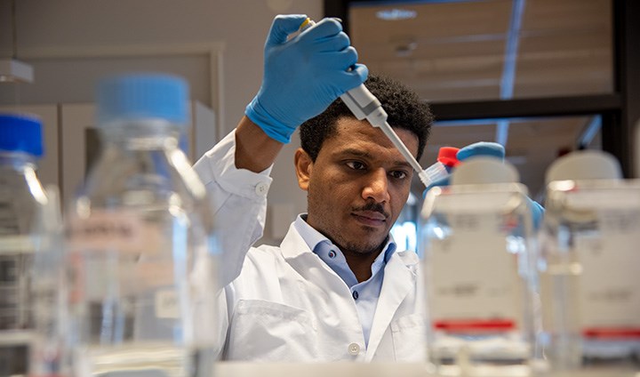 Scientist Mulugeta Zegeye in a laboratory at Örebro University. He is looking at a test tube.