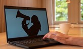 En laptop-dator står på ett bord. På skärmen syns en silhuett av en anonym människa med megafon.