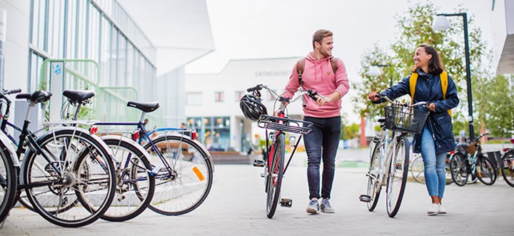 Två studenter leder sina cyklar på campus.