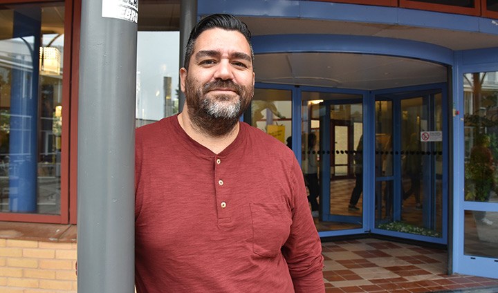 Forskaren Vladimir Cotal San Martin står lutad mot en stolpe utanför Forumhuset vid Örebro universitet.