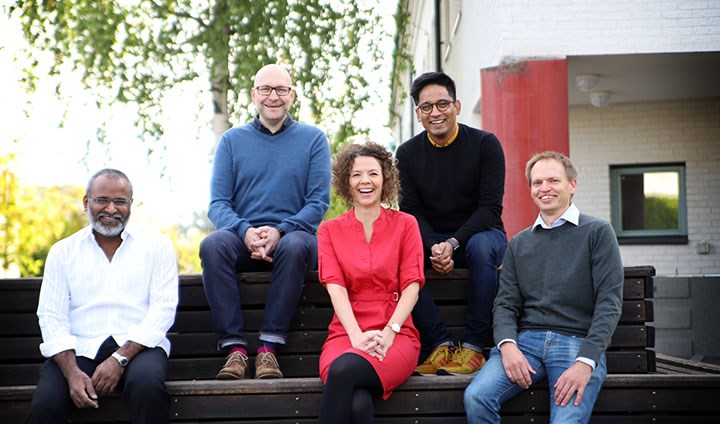 A woman and four men sitting outside on a multi-tiered park bench.