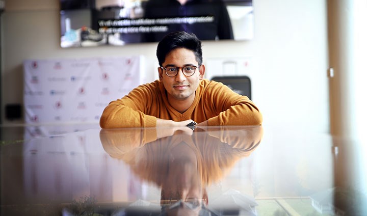 A man sitting at a glass table that is reflecting his image.