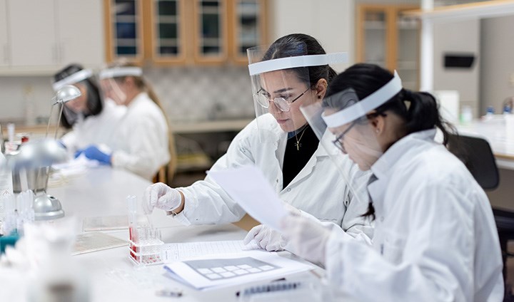 Foto på personer som står i laboratoriemiljö och kollar på provrör.