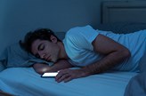 Nattbild. Tonårspojke somnar i sängen med mobiltelefonen i handen.
