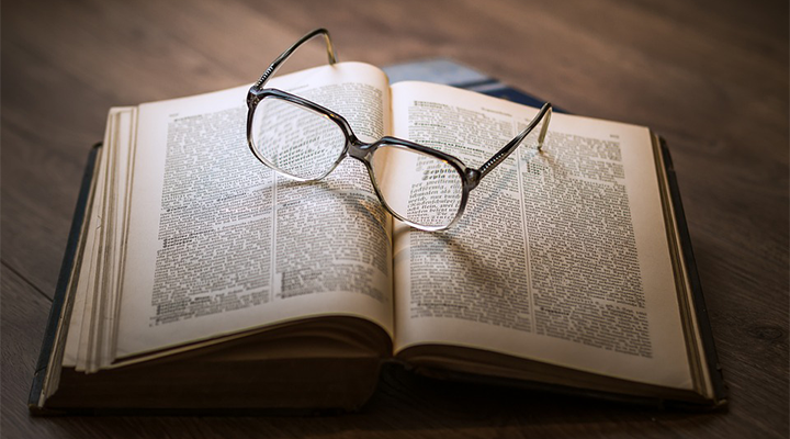 A pair of glasses lie on an open book.