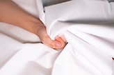 A woman's hand squeezing white sheets