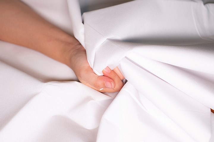 A woman's hand squeezing white sheets