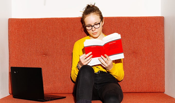 En student sitter i en soffa och läser en bok.