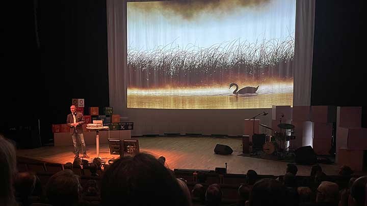 Mattias Klum på scenen i konsertsalen med en bild på en svan. 