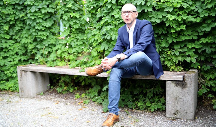 Magnus Hansson sitter på en bänk med grönt bladverk bakom sig. 