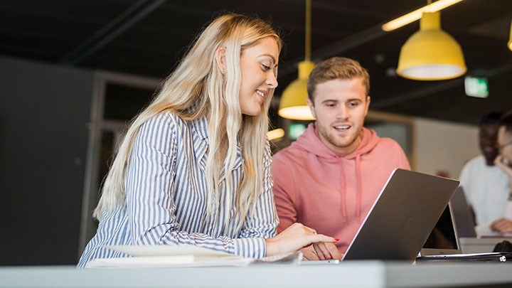 Foto på två studenter som sitter vid ett bord med datorer.