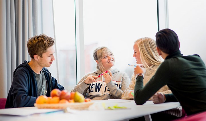 Fyra studenter pratar engagerat runt ett bord.