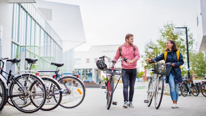 Två studenter går med cyklar på Campus Örebro.
