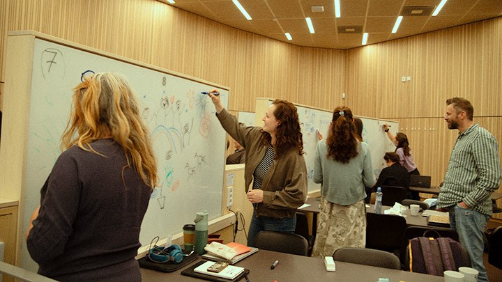 Olika grupperingar av deltagarna på kursen ritar på whiteboards. En man tittar på.