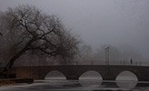 En bro i dimma. En kvinna går över bron.