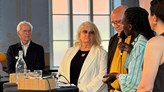 Fem personer står på rad i samtal. En kvinna har en mikrofon i handen. 