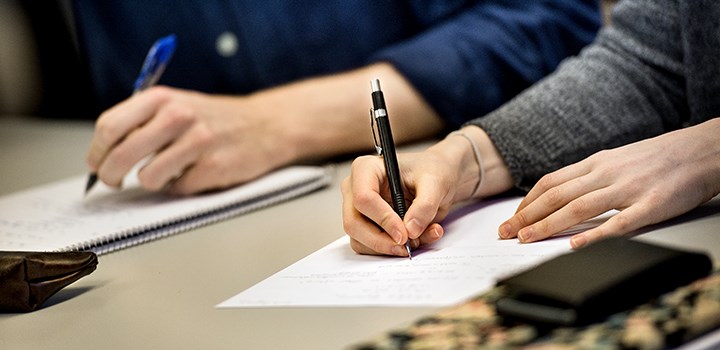 Photo of hands writing on white papers.