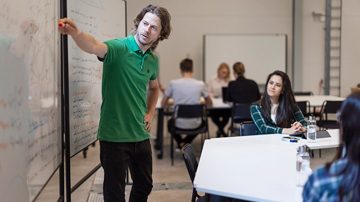 En man står och föresläer vid en whiteboard.