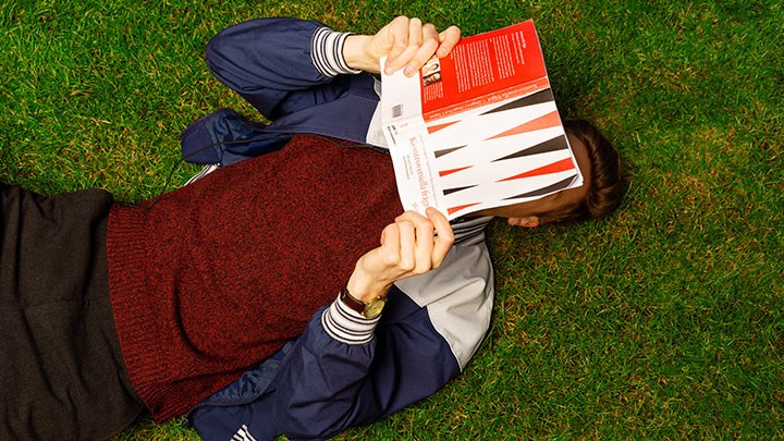 En student ligger och läser i gräset.