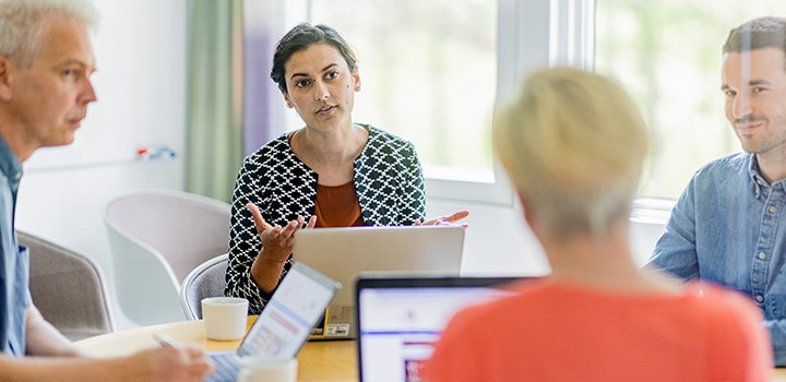 Foto på fyra personer som sitter runt ett bord med datorer.
