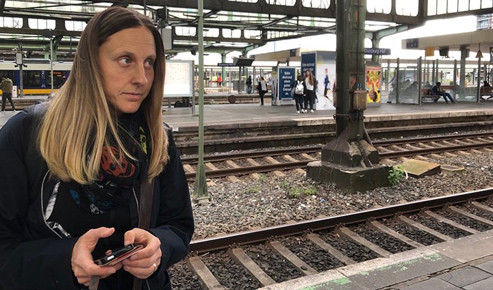 Sara Edlund står med en mobiltelefon i handen och väntar på tåget. Hon spanar ut längs rälsen. I bakgrunden syns en tysk järnvägsstation.