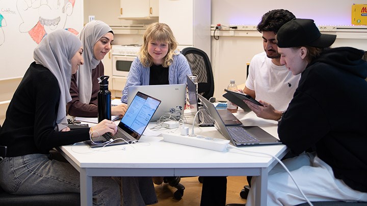 Fem studenter sitter runt ett bord med datorer.