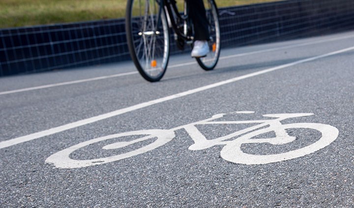 En målad cykelsymbol på en cykelbana. I bakgrunden syns en cyklist.
