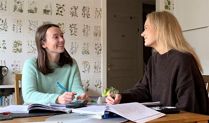 Studenterna Moa Aronsson och Amanda Erensjö pluggar tillsammans vid ett köksbord.