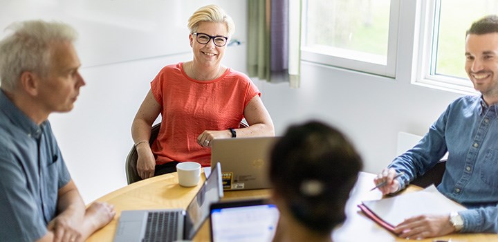 Foto på fyra personer som sitter i ett möte runt ett bord med datorer på.