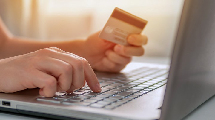 A photo of hands on a keybord holding a credit card.