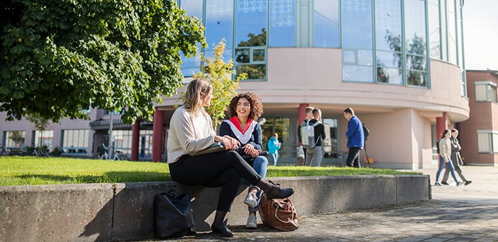 Foto på två personer som sitter på en stenmur med huvudbibliotekets byggnad i bakgrunden.
