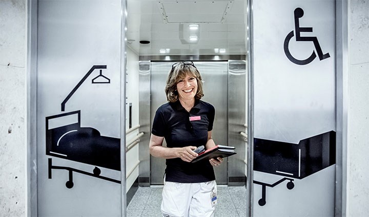 En hälso- och sjukvårdskurator i sjukhuskläder som kliver ur en hiss i sjukhusmiljö.