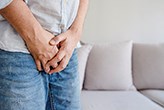 Young man isolated over white background. Cut view low part body. Man holds both hands on crotch. 