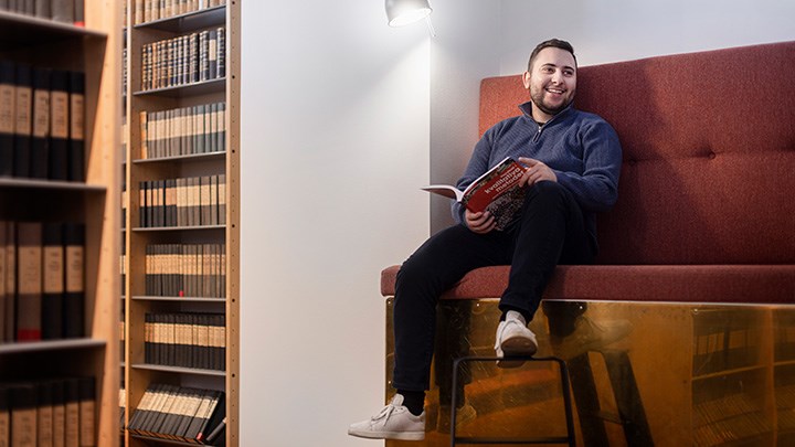 En person ligger på en gräsmatta och läser en bok
