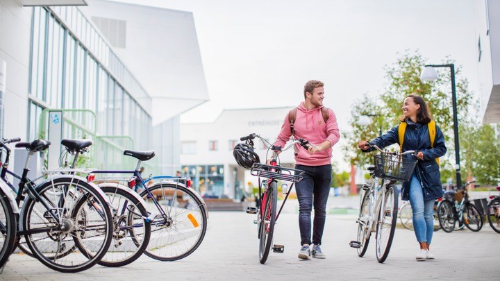 Två studenter går med sina cyklar på campus.