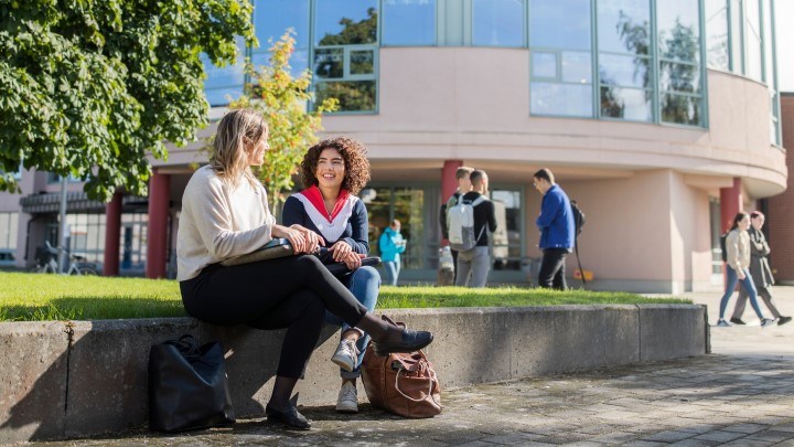 Två kvinnliga studenter på en bänk utanför universitetets bibliotek