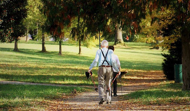 Två äldre människor promenerar i parken. 