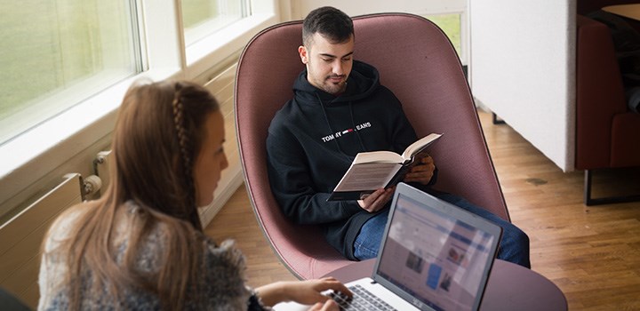 Två personer sitter med en dator respektive en bok i varsin fårölj.
