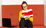 En student i en röd soffa läser bok.