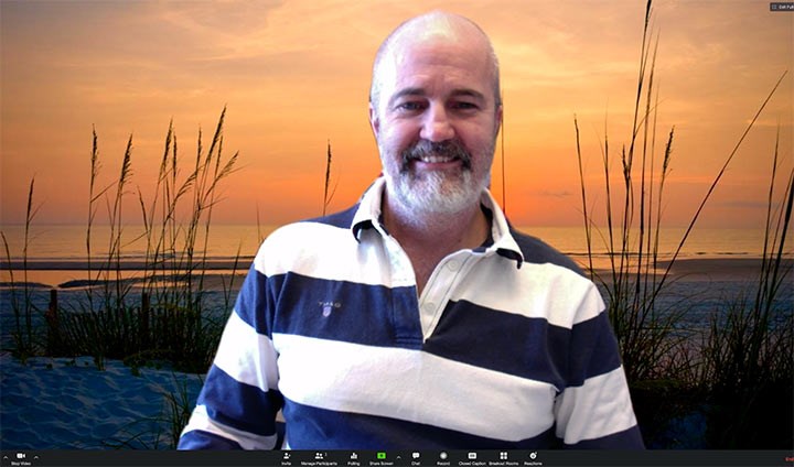 A man in a striped shirt in front of a fake background that is a bunch of reeds.