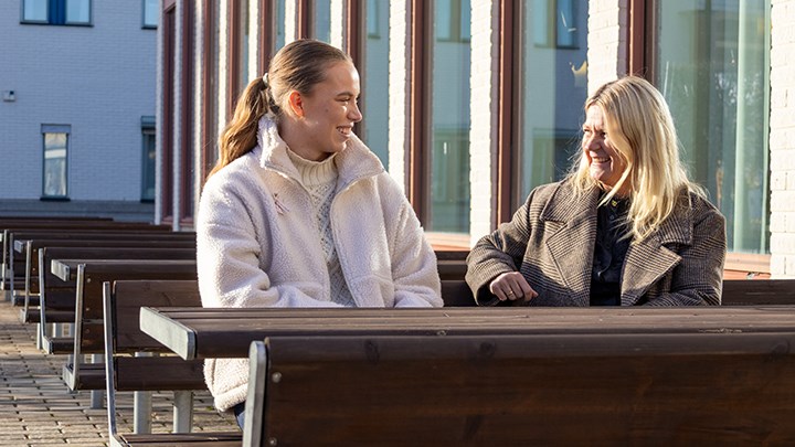 Ebba Löfgren och Karin Blomberg sitter på en bänk med ett bord framför sig.