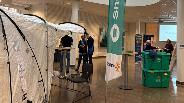 Bild från mässan på tält och lådor med några människor som minglar.