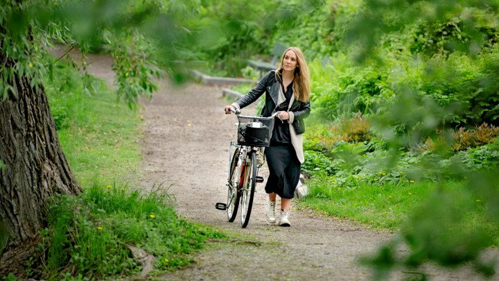 Kvinna leder en cykel på en gångstig bland grönska