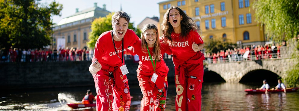 Tre studenter i röda studentoveraller framför en bro utanför Örebro slott.