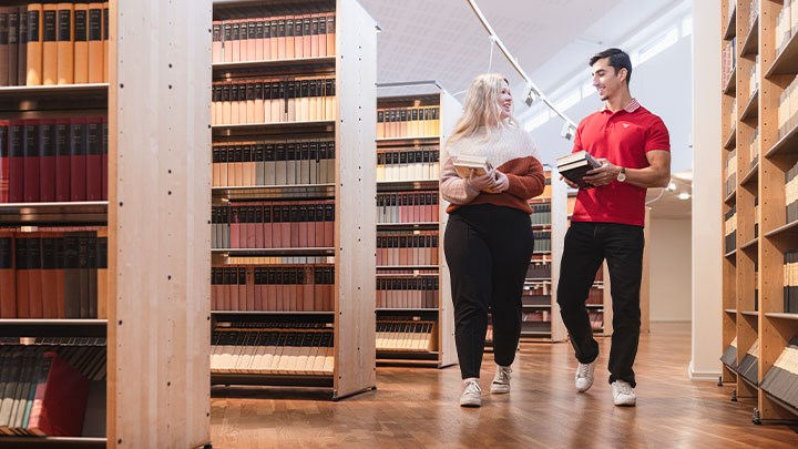 Två personer håller i böcker och går i huvudbiblioteket.